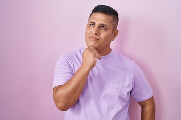 Young hispanic man standing over pink background with hand on chin thinking about question, pensive expression. smiling and thoughtful face. doubt concept.