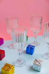 Faceted champagne glasses for a party and small gifts on a pink and blue background
