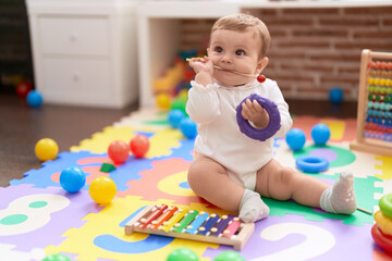 Adorable toddler bitting xylophone stick sitting on floor at kindergarten