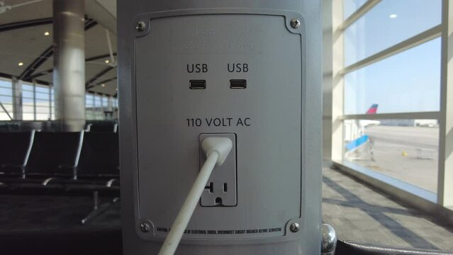 Plugging in  a laptop from a charging station at an airport near the seats while you wait for a flight.