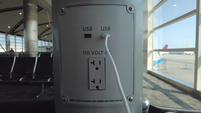 plugging in the cell phone charger from a charging station at an airport near the seats while you wait for a flight.