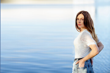 Banner with a blue lake background and a beautiful brunette girl in a white t-shirt and jeans. Casual wear. Casual style. Summer concept. Copy space on the left