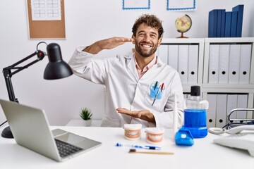 Young hispanic dentist man working at medical clinic gesturing with hands showing big and large size sign, measure symbol. smiling looking at the camera. measuring concept.