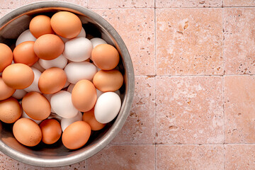 Eggs in metallic bowl on beige background with copy space. Top view of raw brown eggs and white eggs with chicken feathers.