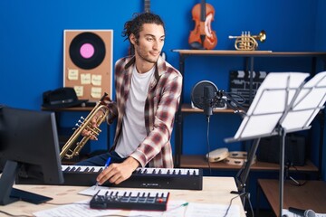 Fototapeta na wymiar Young hispanic man musician composing song holding trumpet at music studio