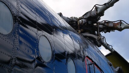 Shot from below from side blue helicopter fuselage and articulated main rotor. Dark blue helicopter...