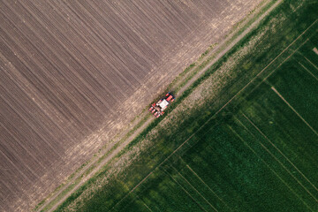 Aerial shot of agricultural tractor with crop seeder attached driving along dirt road through plowed fields, drone pov