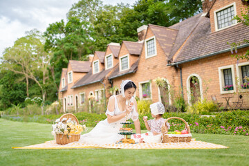 Soft portrait of asian young woman and her daughter relaxing on a mat with picnic baskets in...