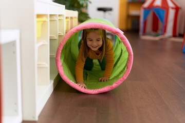 Adorable hispanic girl crawling inside tunnel toy at kindergarten