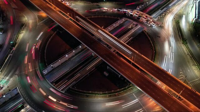 Time-lapse of car traffic transportation on road at junction intersection, 4K. Aerial view of road interchange or highway intersection with busy urban traffic speeding on the road at night, IoT GPS 5g