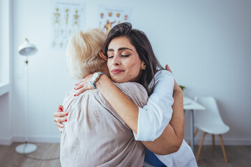 Shot of a young woman doctor hugging her senior patient during a consultation. The proud home...