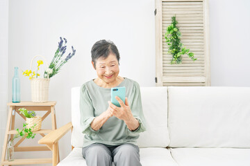 家で笑顔でスマホを使う高齢者女性