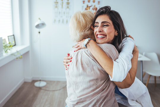 Caring young medical doctor hugging senior patient. Happy woman hugging doctor, good test results, recovery and remission, gratitude. Home healthcare nurse embraces her patient