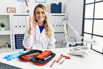 Young beautiful doctor woman with reflex hammer and medical instruments smiling positive doing ok sign with hand and fingers. successful expression.
