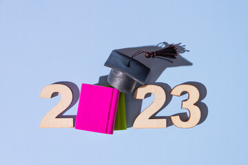 Class of 2023 concept. Numbers 2023 with black graduated cap and books top view on colored background.