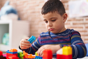 Adorable hispanic toddler playing with construction blocks sitting on table at kindergarten