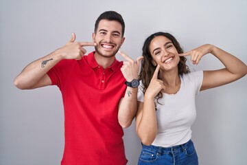 Young hispanic couple standing over isolated background smiling cheerful showing and pointing with fingers teeth and mouth. dental health concept.