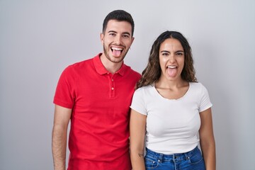 Obraz premium Young hispanic couple standing over isolated background sticking tongue out happy with funny expression. emotion concept.
