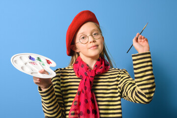 Fototapeta premium Young artist. A girl with a palette of colors in a bright red beret and with a brush on a blue background. close-up portrait