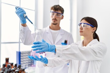 Man and woman partners wearing scientist uniform holding test tube and pipette at laboratory