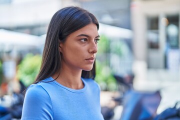 Young beautiful hispanic woman looking to the side with serious expression at coffee shop terrace