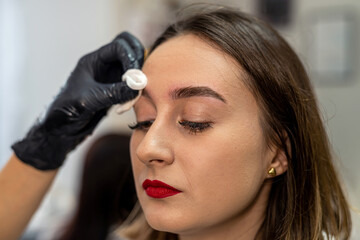 beautiful young client is wiping her eyebrows after painting them.