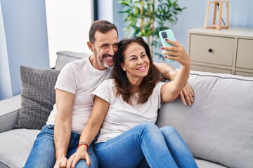 Obraz premium Middle age man and woman couple make selfie by the smartphone sitting on sofa at home