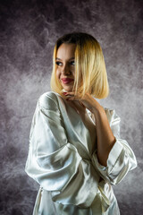 Gorgeous young woman with hairdo in silk robe looking dreamily at camera in home style.