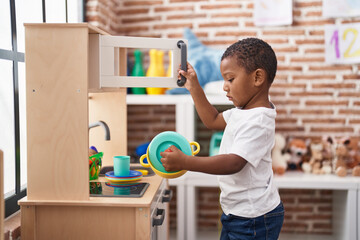 African american boy playing with play kitchen standing at kindergarten