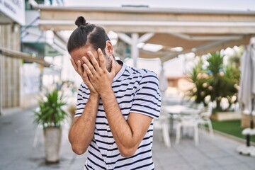 Young hispanic man with beard outdoors at the city with sad expression covering face with hands while crying. depression concept.