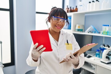 Young beautiful latin woman scientist using touchpad reading document at laboratory