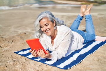 Middle age woman using touchpad lying on towel at seaside