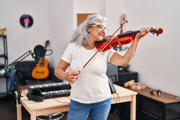 Middle age woman musician playing violin at music studio - obrazy, fototapety, plakaty