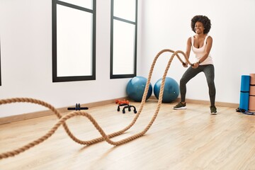 Young african american woman smiling confident training with battle rope at sport center