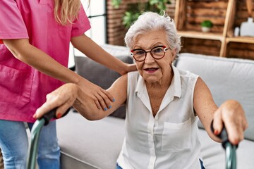Senior grey-haired woman patient supported for nurse and walker at geriatric