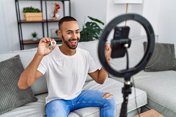 African american man recording vlog tutorial about bitcoin with smartphone at home celebrating...