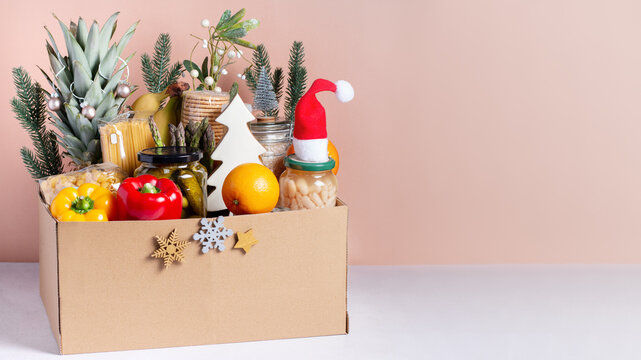 Canned food, pasta, fruits and vegetables in a box for donation decorated for Christmas, charity concept
