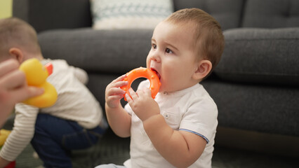 Adorable toddler bitting plastic hoop sitting on floor at home © Krakenimages.com