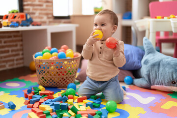 Adorable toddler bitting ball sitting on floor at kindergarten