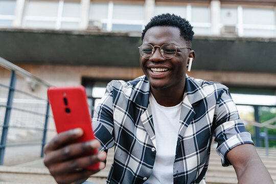 Excited young African man using mobile phone and earphones for online video call