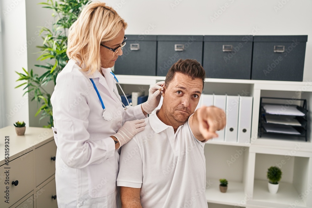 Wall mural Hispanic man getting medical hearing aid at the doctor pointing with finger to the camera and to you, confident gesture looking serious