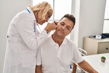 Middle age man and woman doctor and patient examining ear having medical consultation at clinic
