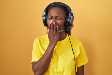 African american woman listening to music using headphones bored yawning tired covering mouth with hand. restless and sleepiness.