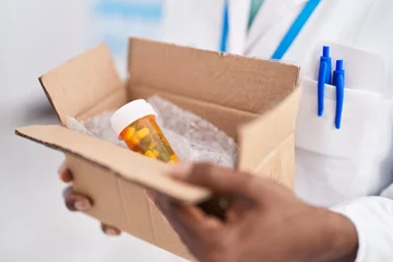 Wandcirkels aluminium African american woman pharmacist holding package with pills bottle at pharmacy © Krakenimages.com
