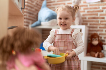 Adorable caucasian girl playing with play kitchen standing at kindergarten