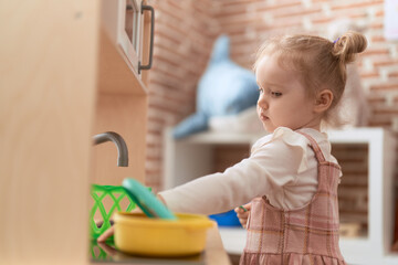 Adorable caucasian girl playing with play kitchen standing at kindergarten