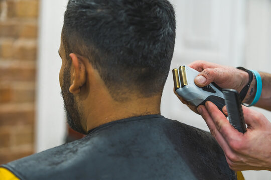 Rear close up view of barber hands using hair clipper for a male haircut . High quality photo
