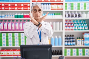 Middle age woman with tattoos working at pharmacy drugstore rejection expression crossing arms...