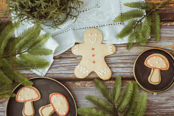 Overhead view of gingerbread man and gingerbread mushroom cookies on a wooden table with a houseplant, fir branches and a lace tablecloth