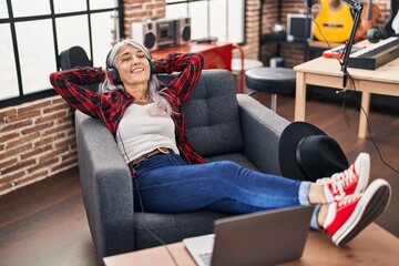 Obraz premium Middle age grey-haired woman artist listening to music relaxed on sofa at music studio